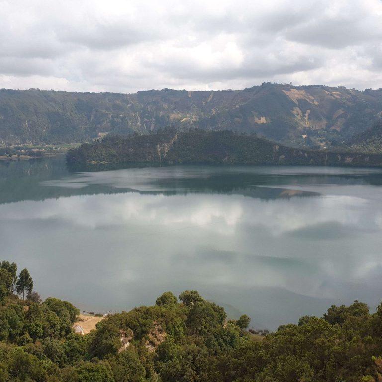 Wonchi Crater Lake ringed by forested crater walls, with cloud reflected on the water