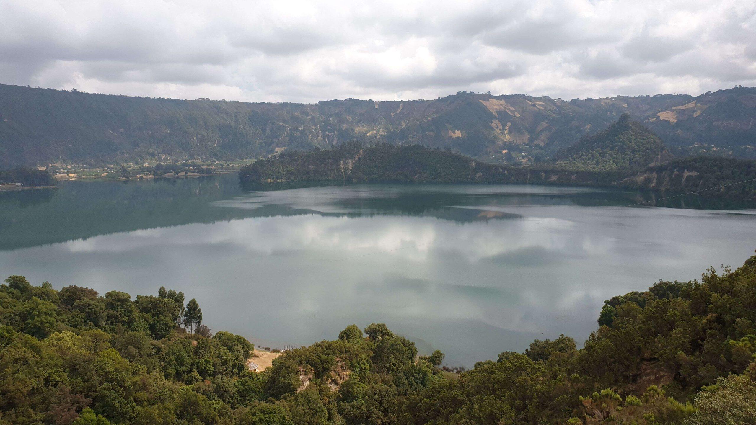Wonchi Crater Lake ringed by forested crater walls, with cloud reflected on the water