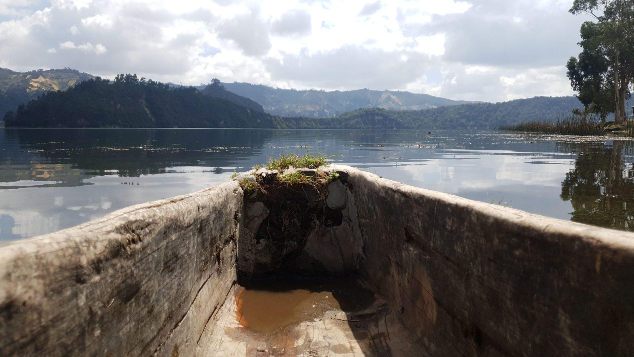 The view forward from inside a dugout canoe crossing Wonchi Crater Lake, still water ahead and the forested crater walls rising on the far side