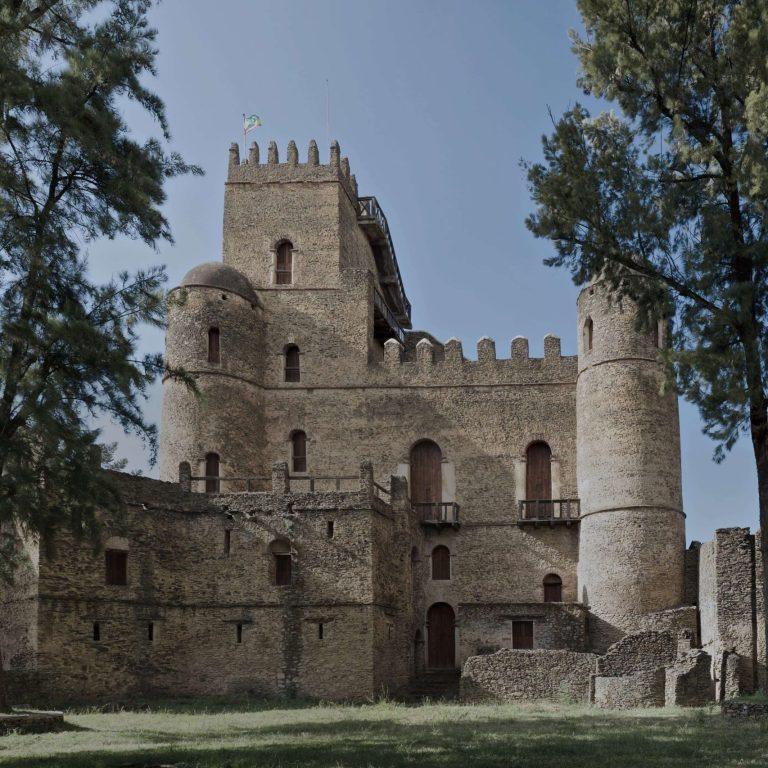 Fasilides castle in the Royal Enclosure at Gondar, a stone tower with crenellations and a domed turret, framed by tall trees
