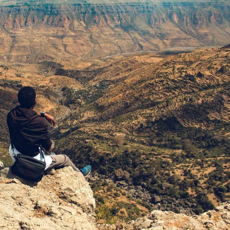 A person sitting on a rocky clifftop above the Jemma River gorge near Debre Libanos, looking out over terraced slopes falling away to the valley floor
