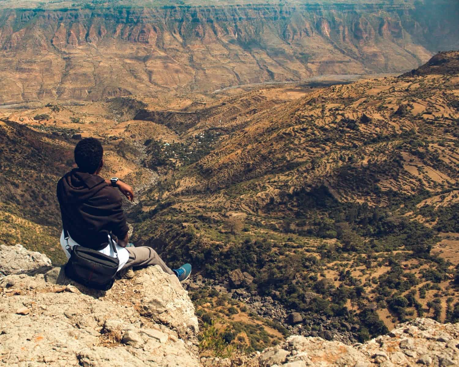A person sitting on a rocky clifftop above the Jemma River gorge near Debre Libanos, looking out over terraced slopes falling away to the valley floor