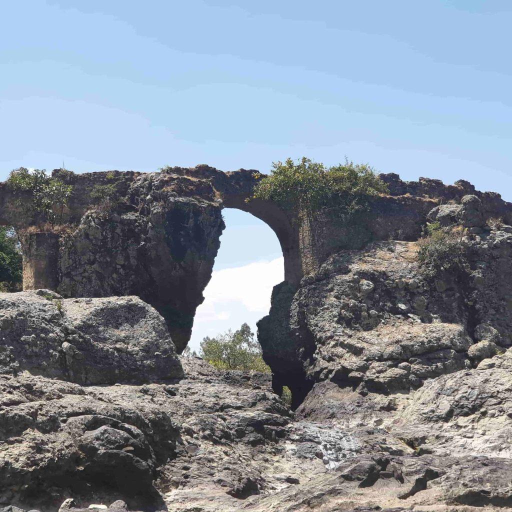 The Portuguese Bridge near Debre Libanos, a weathered stone arch springing from a squared masonry pier and spanning a rocky gorge, with scrub growing along its top