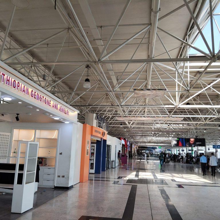 The airside concourse at Bole airport, with a lit Ethiopian gemstone and jewellery unit on the left, further shops along the walkway and seated passengers waiting near the gates