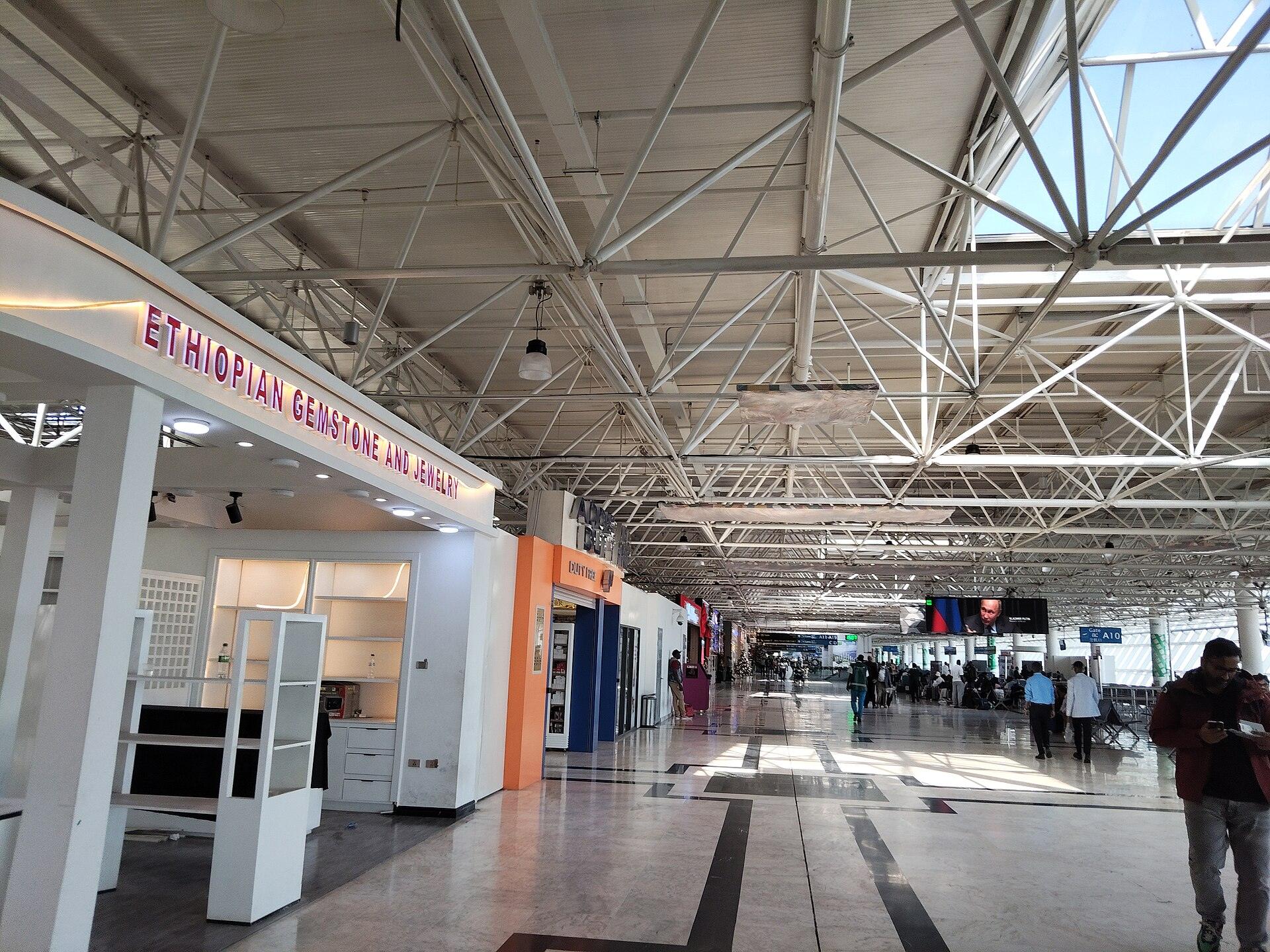 The airside concourse at Bole airport, with a lit Ethiopian gemstone and jewellery unit on the left, further shops along the walkway and seated passengers waiting near the gates