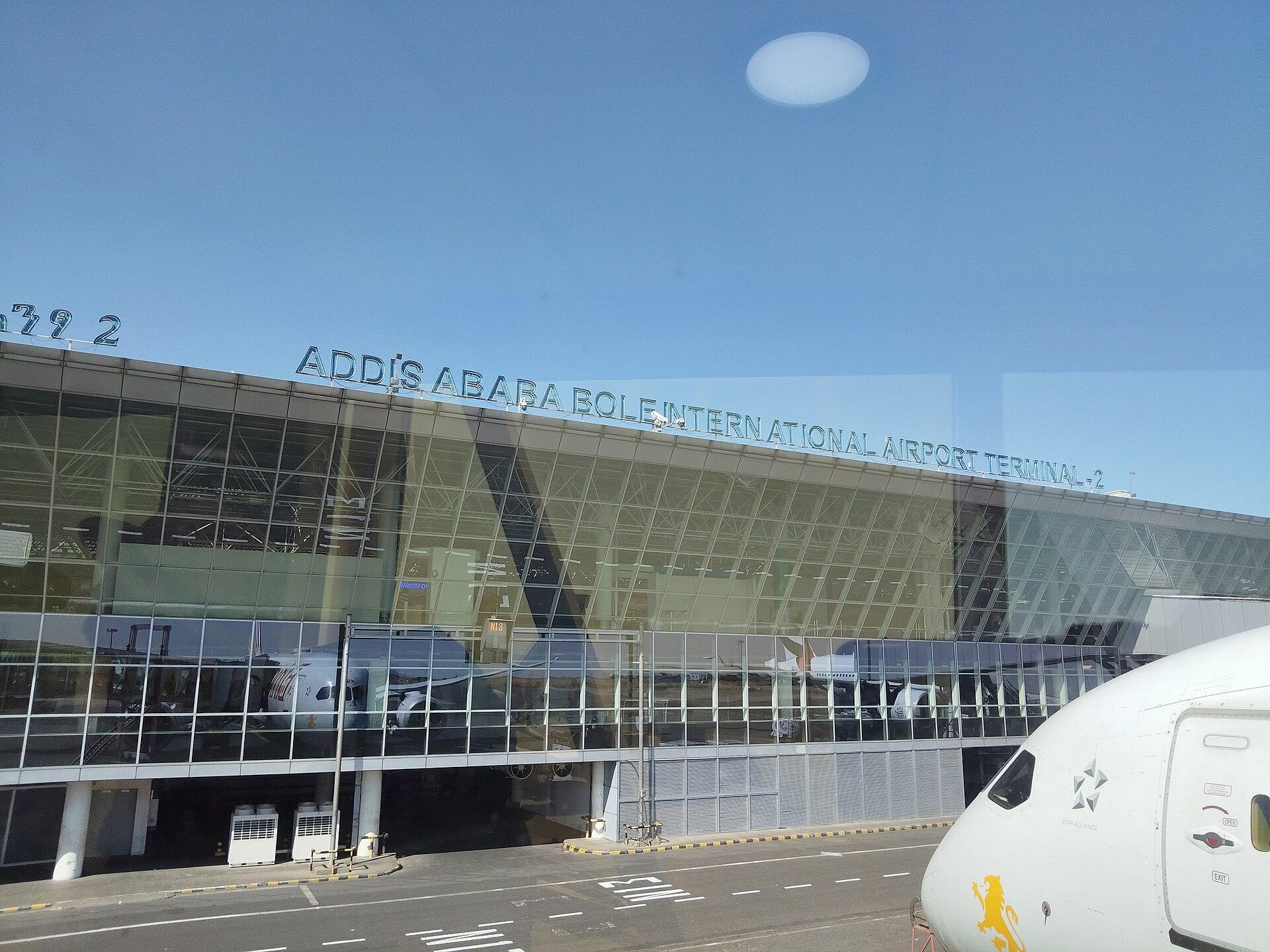 The glass frontage of Addis Ababa Bole International Airport Terminal 2, with the terminal name across the roofline and the nose of an Ethiopian Airlines aircraft on the apron alongside