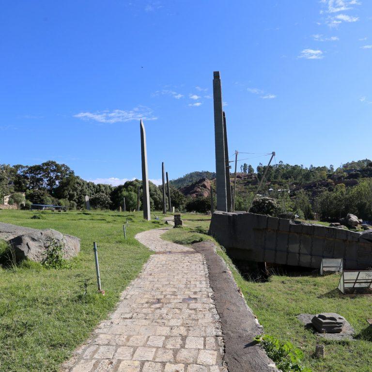 The northern stelae field at Aksum, with carved granite stelae standing against a blue sky and the broken sections of the fallen Great Stele lying on the right