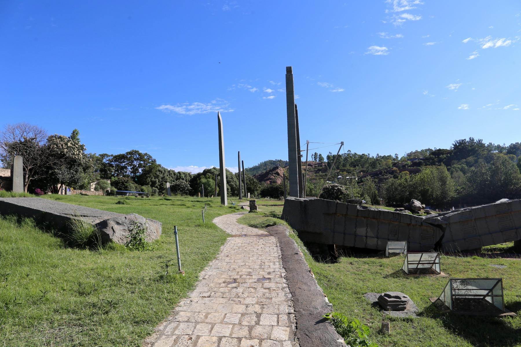 The northern stelae field at Aksum, with carved granite stelae standing against a blue sky and the broken sections of the fallen Great Stele lying on the right
