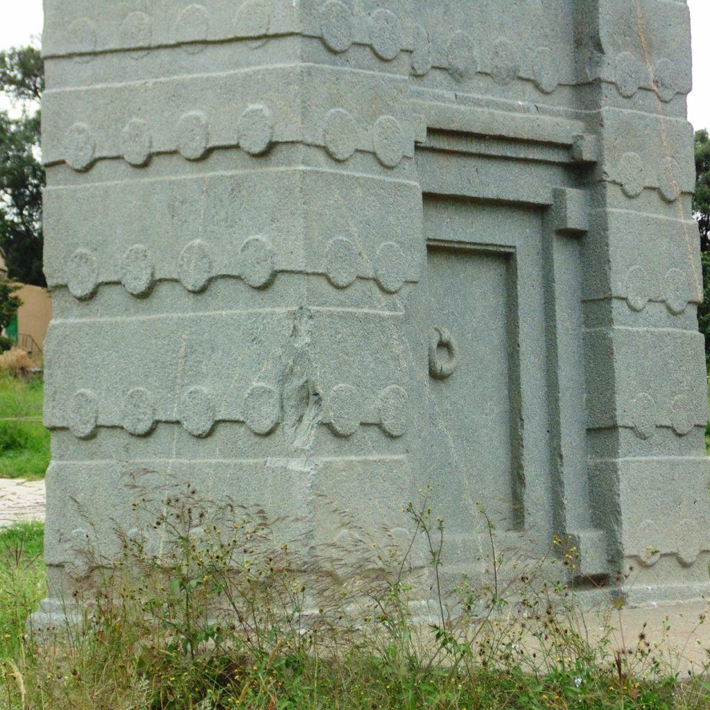 The base of a granite stele at Aksum carved with a false door complete with a stone door-ring, and rows of carved beam ends above it imitating the storeys of a building