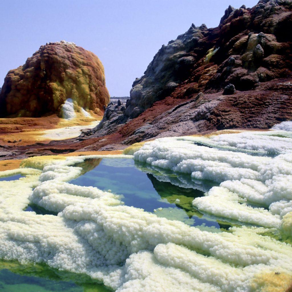 Acid pools in green and blue ringed by white salt crusts and orange mineral mounds at Dallol in the Danakil Depression