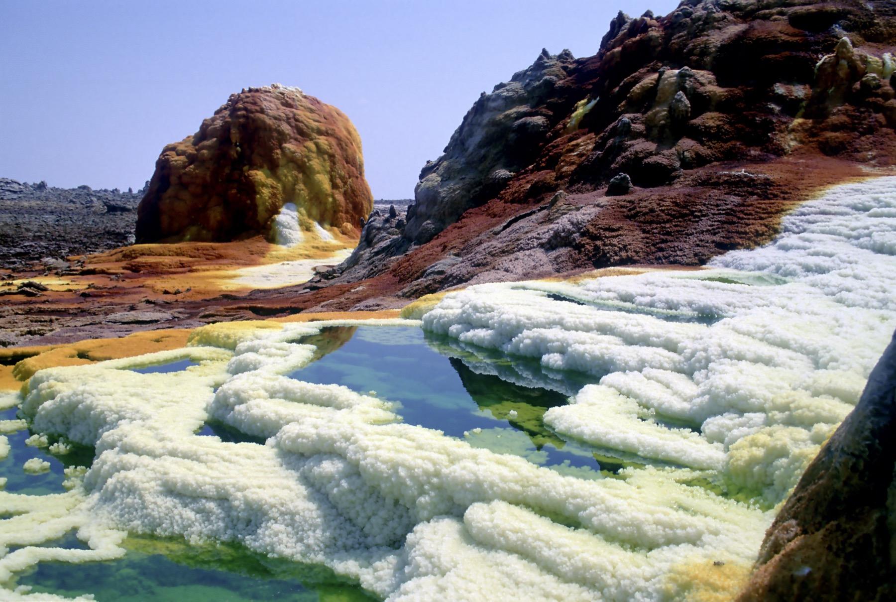 Acid pools in green and blue ringed by white salt crusts and orange mineral mounds at Dallol in the Danakil Depression