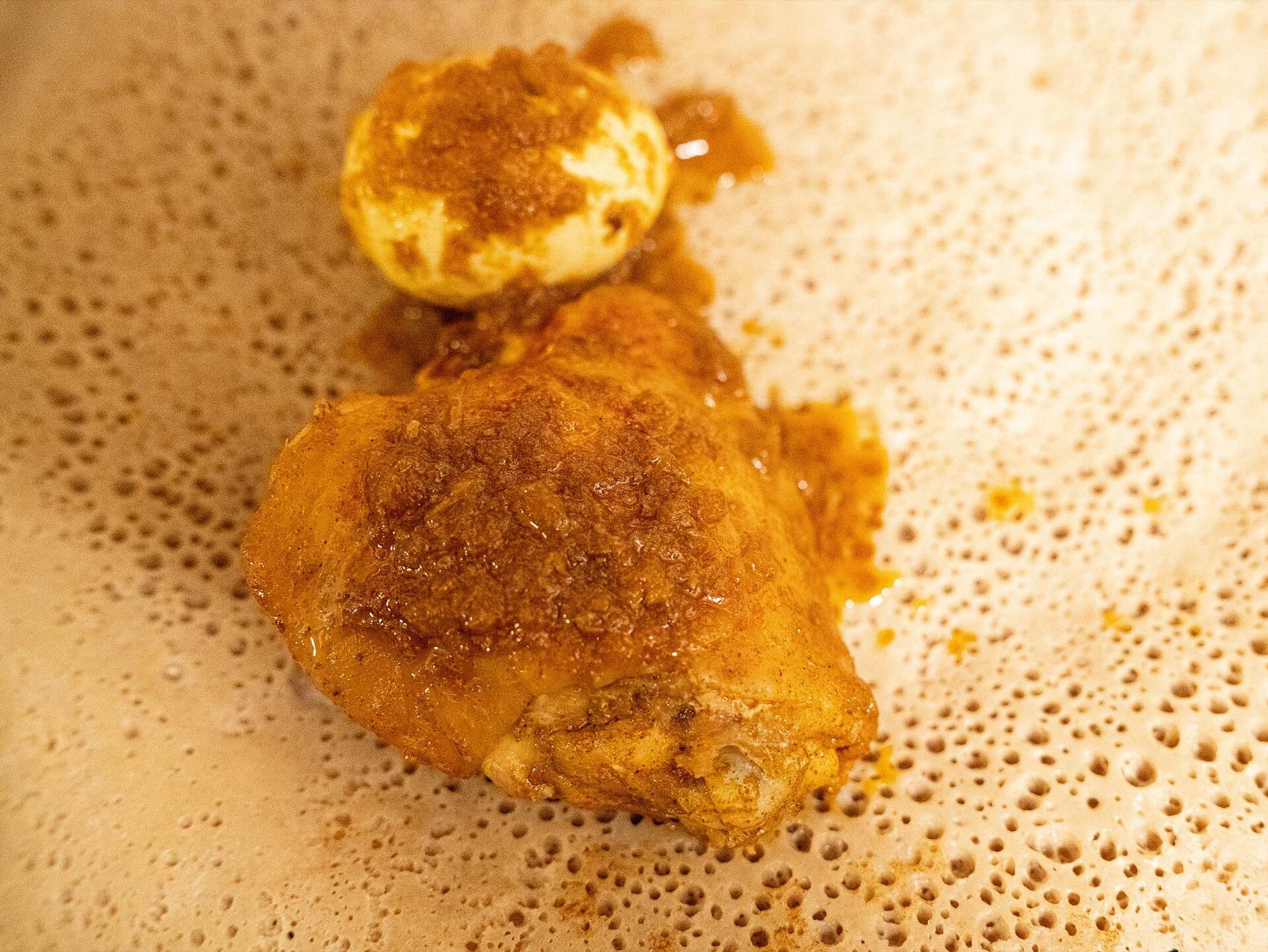A piece of chicken in deep red berbere sauce with a hard-boiled egg beside it, served on injera whose fermentation holes are clearly visible