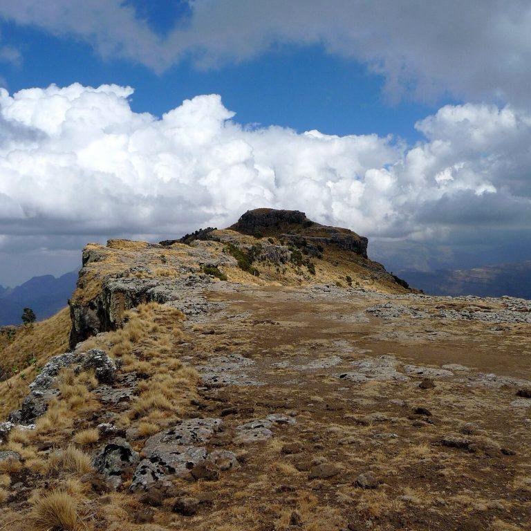 The rocky summit ridge of Imet Gogo in the Simien Mountains, tussock grass and basalt outcrops in the foreground with tall cumulus cloud above and the escarpment falling away into haze