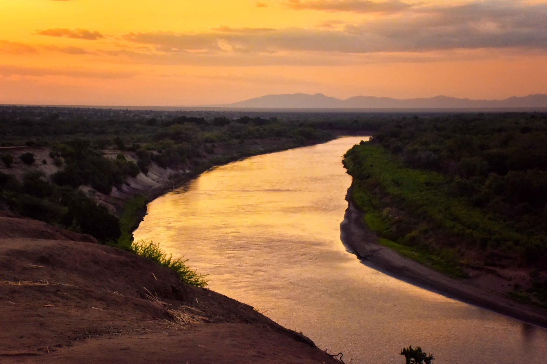 The Omo River curving through dry scrub at sunset, seen from a high bank, with low hills on the horizon