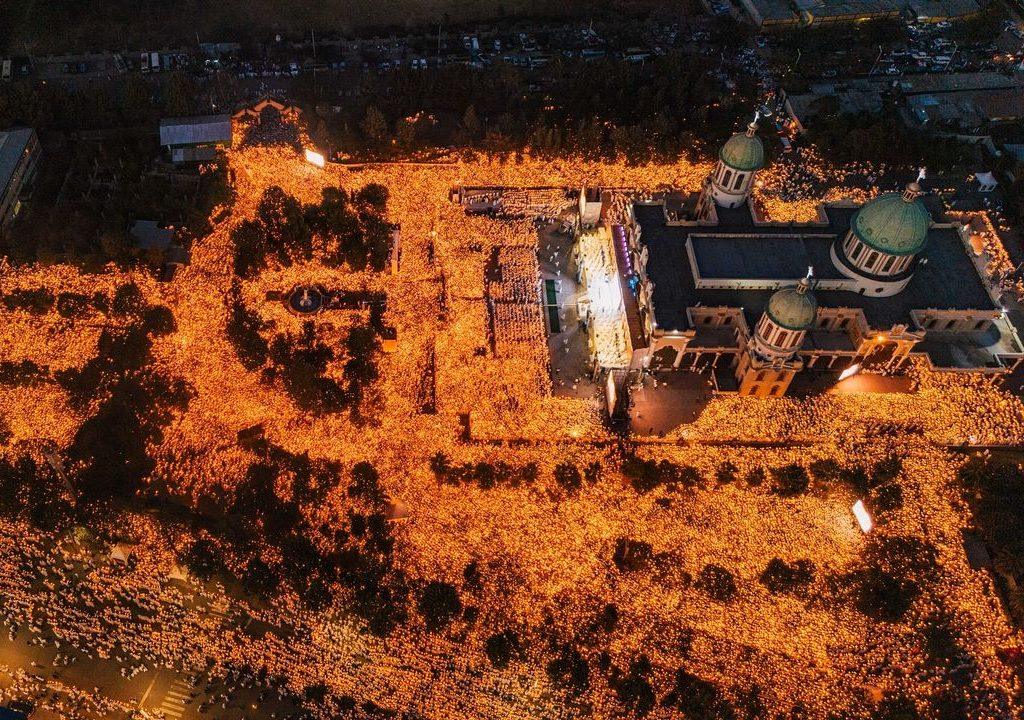 Aerial view at dusk of a vast crowd holding candles filling the grounds and streets around a large cathedral with green domes in Addis Ababa on Ethiopian Christmas Eve