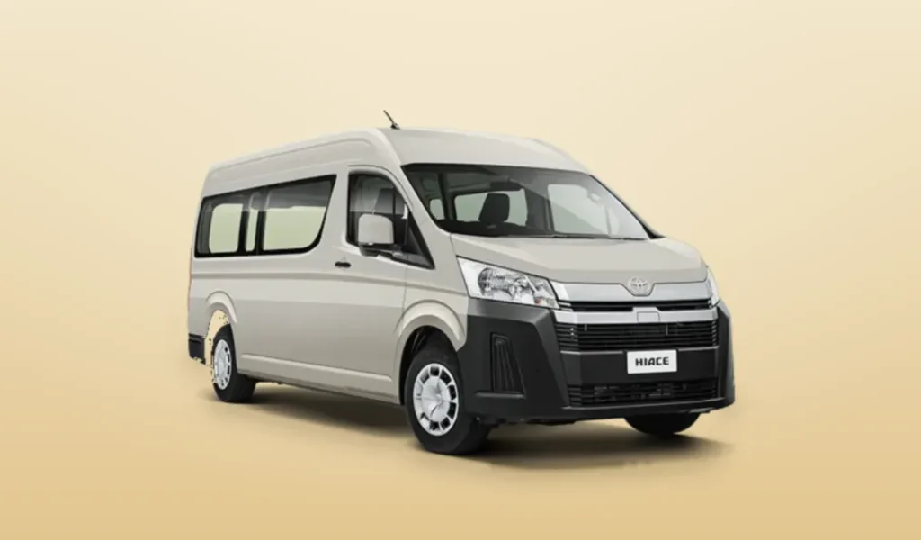 A silver Toyota Hiace high-roof minibus seen from the front three-quarter angle against a plain cream background