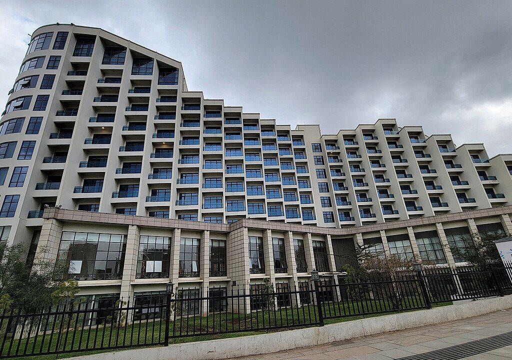 The curved multi-storey cream facade of the Ethiopian Skylight Hotel with rows of balconies and blue-tinted windows behind a black railing, under a grey sky