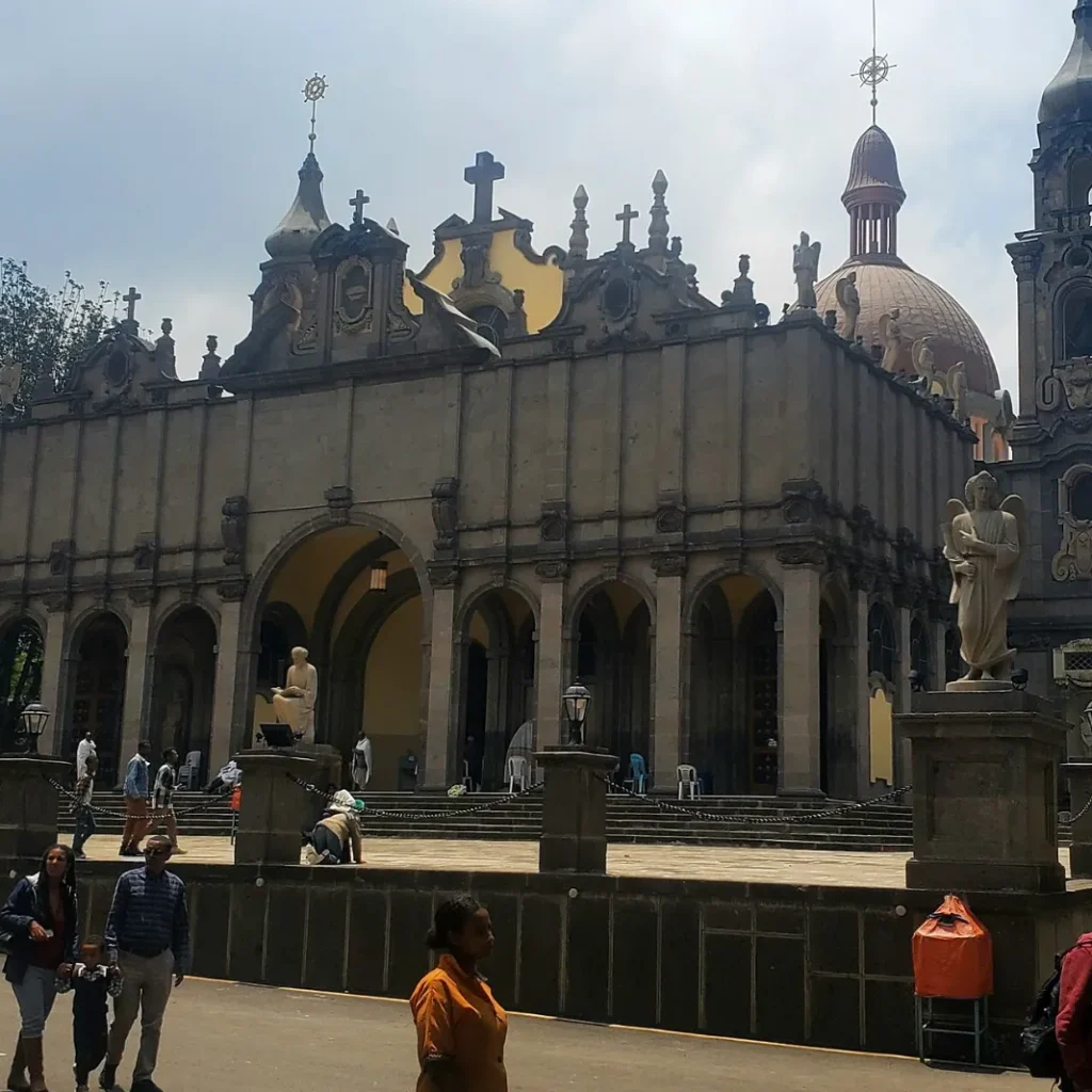 The stone facade of Holy Trinity Cathedral in Addis Ababa with arched doorways, statues and a domed tower, as visitors walk across the courtyard in front