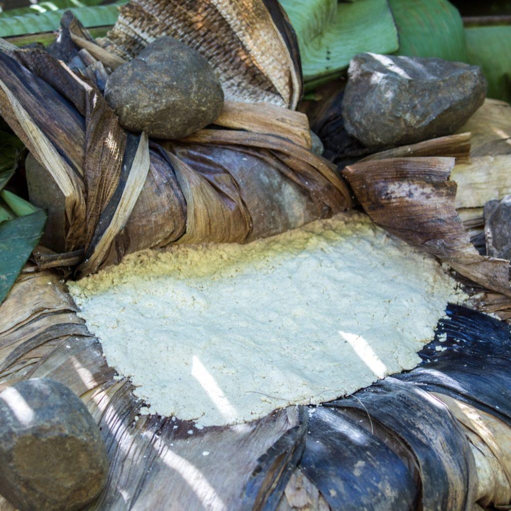 A flat round of pale kocho dough spread on dried enset leaves and weighted at the edges with stones